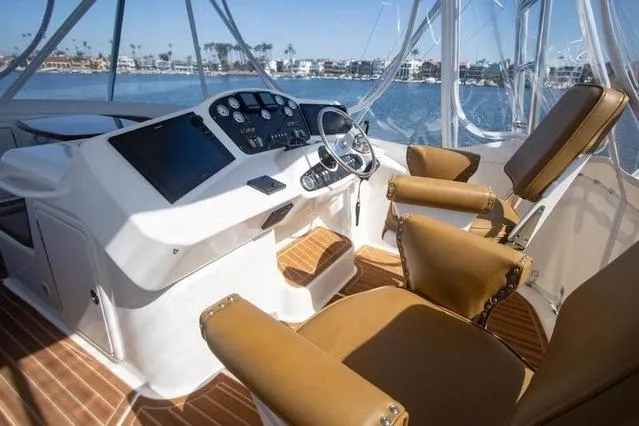 Slide: The Image of 2003 Riviera 4700 Sport Yacht helm with leather seats and modern controls, overlooking marina. - 34