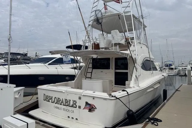 Slide: The Image of 2003 Riviera 4700 Sport Yacht docked at marina, rear view with ladder and name "Deplorable." - 73