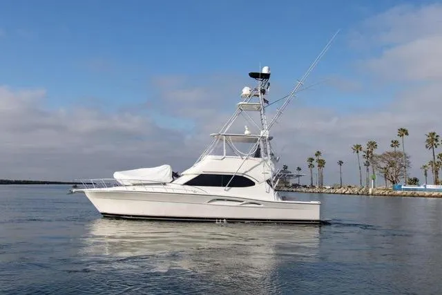 Slide: The Image of 2003 Riviera 4700 Sport Yacht cruising on calm waters near a palm-lined shore. - 9