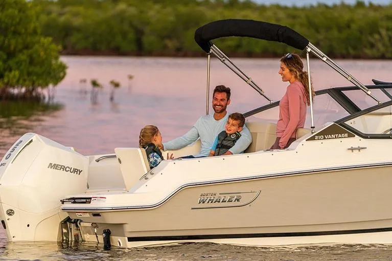 Slide: The Image of Family enjoying a 2024 Boston Whaler 210 Vantage boat on a serene lake. - 22