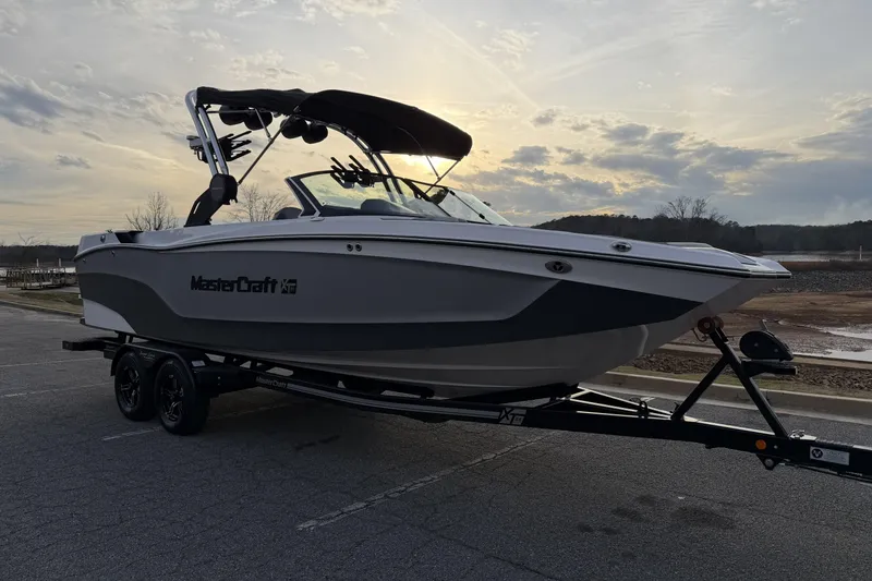 Slide: The Image of 2023 MasterCraft XT24 boat on trailer at sunset, parked near a lake. - 5