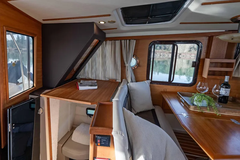Slide: The Image of 2014 Ranger Tug R-31 CB interior with cozy seating, wooden table, and scenic window view. - 11