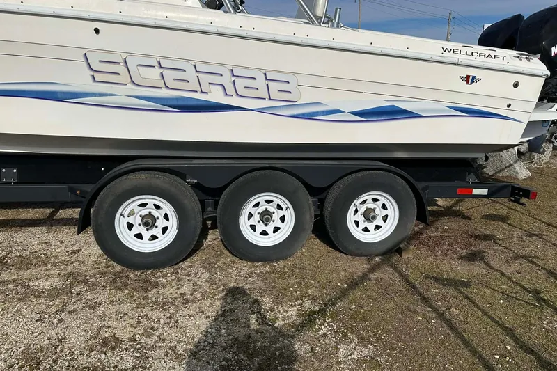 Slide: The Image of 1995 Wellcraft 302 Scarab Sport boat on trailer, featuring bold graphics and triple-axle wheels. - 20