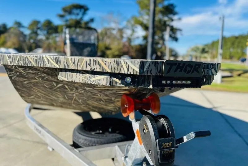 Slide: The Image of Camouflage-patterned Thor 1900 boat on trailer, 2026 model, outdoors with trees in background. - 3