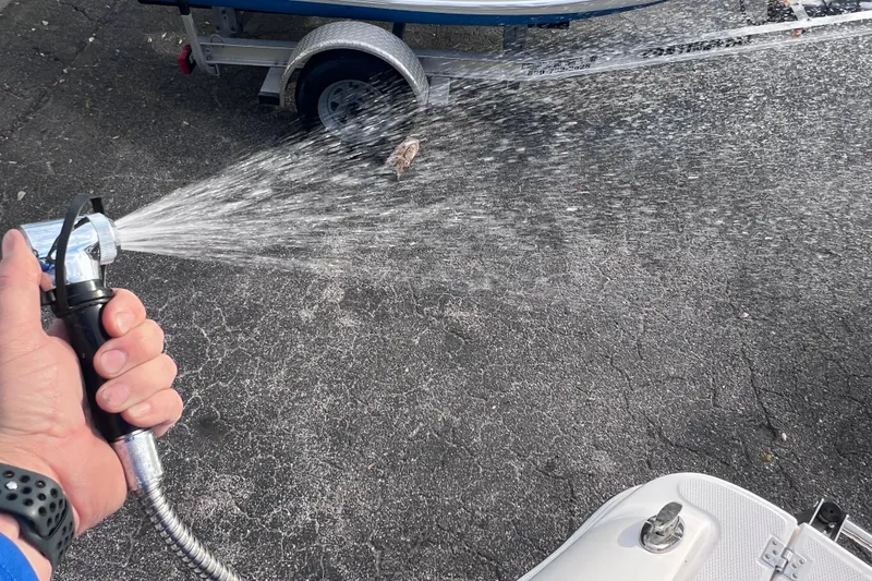 Slide: The Image of Hand spraying water near a 2023 Robalo R222 Explorer boat on a trailer. - 21