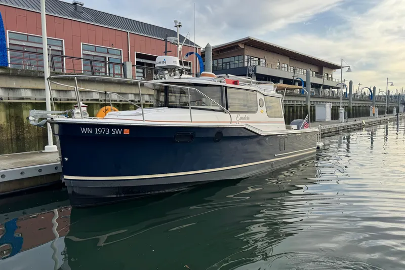 The Image of 2021 Ranger Tugs R-27 boat docked at a marina with modern buildings in the background. - 0