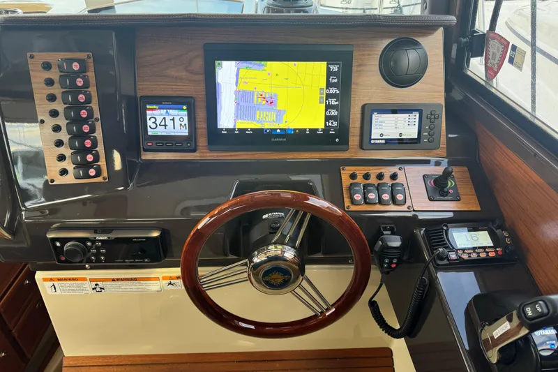 Slide: The Image of 2021 Ranger Tugs R-27 helm with navigation screens, controls, and wooden steering wheel. - 13