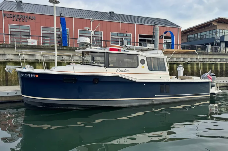 Slide: The Image of 2021 Ranger Tugs R-27 boat docked at marina, with red building in background. - 2