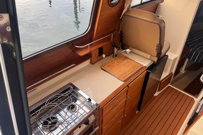 Slide: The Image of 2021 Ranger Tugs R-27 interior kitchen with stove, sink, and wooden cabinetry. - 8