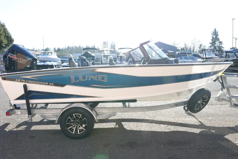 Slide: The Image of 2026 Lund 1875 Crossover XS boat on trailer, side view in a sunny marina. - 5