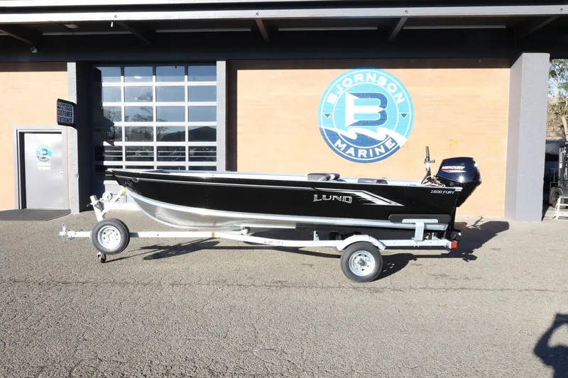 The Image of 2026 Lund 1600 Fury Tiller boat on trailer outside marine dealership. - 1