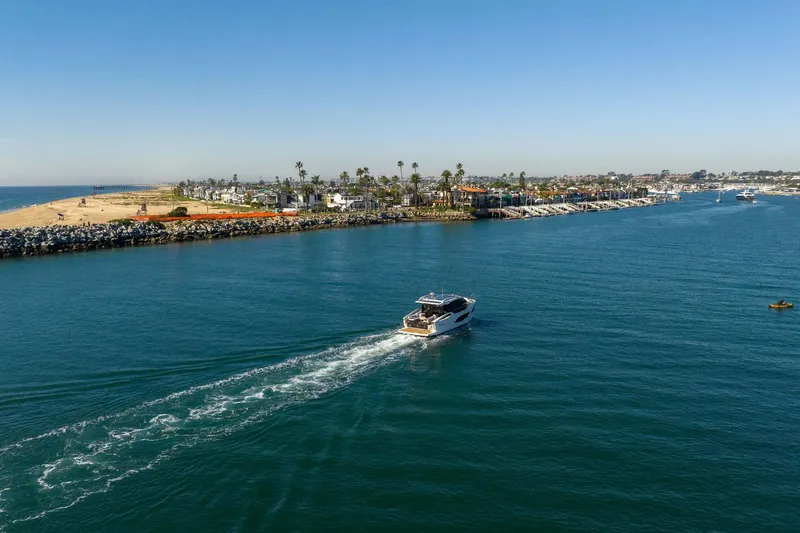 Slide: The Image of A 2026 Absolute 48 Coupe yacht cruising near a coastal town under clear blue skies. - 15