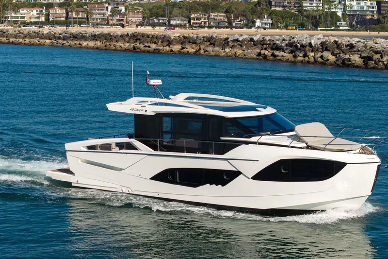 Slide: The Image of 2026 Absolute 48 Coupe yacht cruising on blue water near a rocky shoreline. - 2