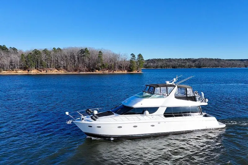 Slide: The Image of 2001 Carver 570 Voyager Pilothouse yacht cruising on a serene lake under clear blue skies. - 2