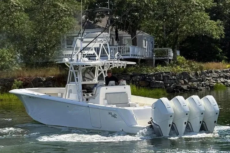 Slide: The Image of 2023 SeaVee 390Z boat with four engines cruising near a rocky shoreline. - 2