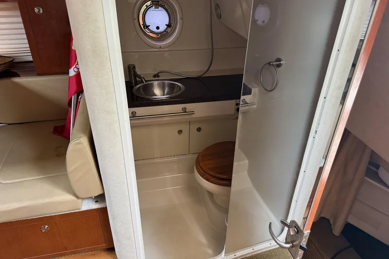 Slide: The Image of 2013 Sea Ray Sundancer 310 bathroom with sink and toilet, featuring a porthole window. - 45