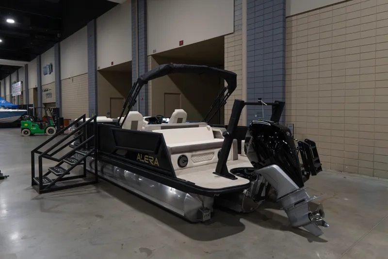 The Image of 2026 Alera M23Q pontoon boat displayed indoors with motor and stairs. - 1