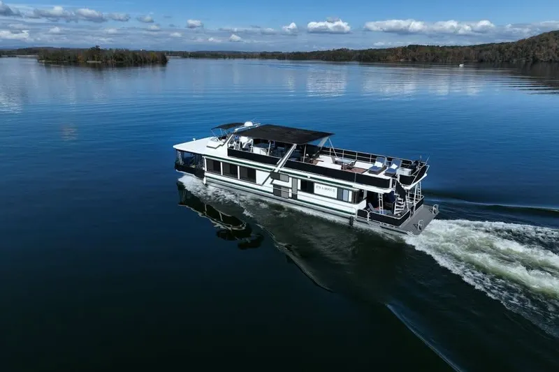 Slide: The Image of 1996 Sumerset 82'x18' Widebody houseboat cruising on a serene lake under a blue sky. - 4
