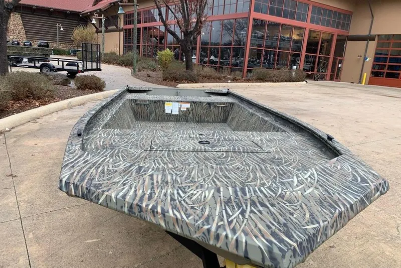 Slide: The Image of 2026 Tracker Grizzly 1648 Utility boat with camouflage design outside a building. - 2