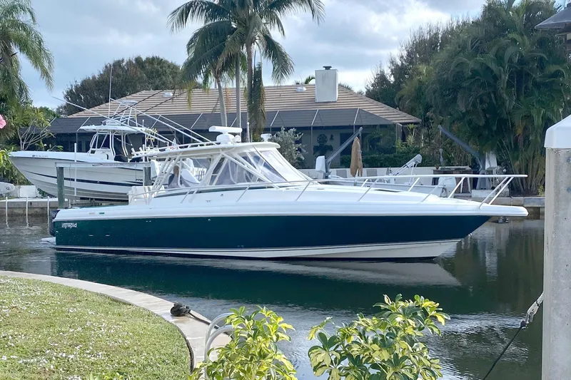 The Image of 2004 Intrepid 377 Walkaround boat docked near palm trees and waterfront home. - 0
