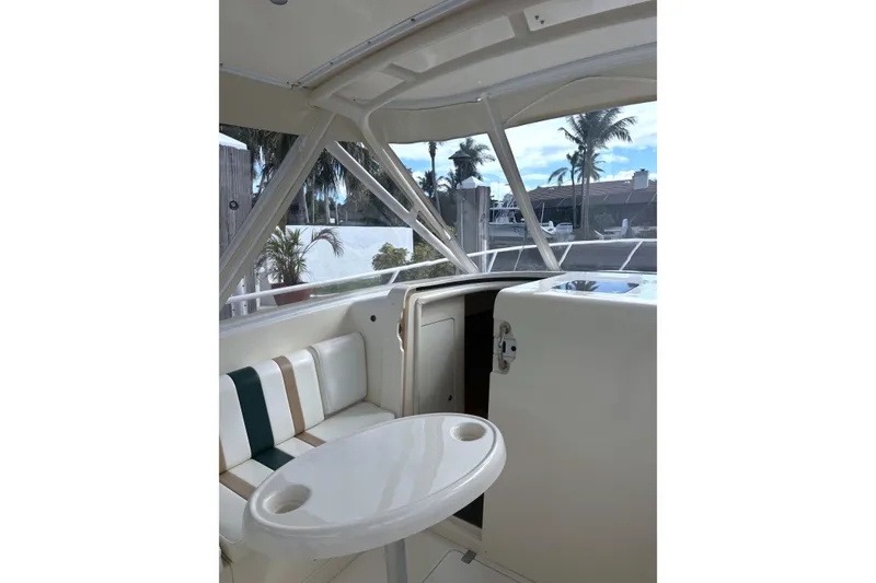 Slide: The Image of 2004 Intrepid 377 Walkaround boat interior with seating and table, featuring a tropical backdrop. - 14