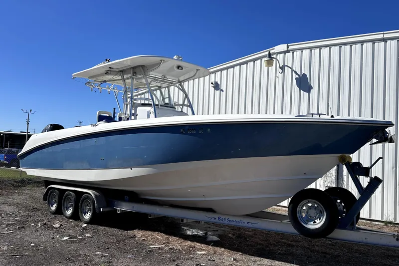 The Image of 2007 Boston Whaler 320 Outrage boat on trailer, parked outdoors under clear blue sky. - 0
