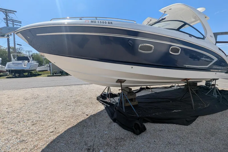 Slide: The Image of 2013 Chaparral 327 SSX boat on stands, blue and white hull, sunny day. - 20