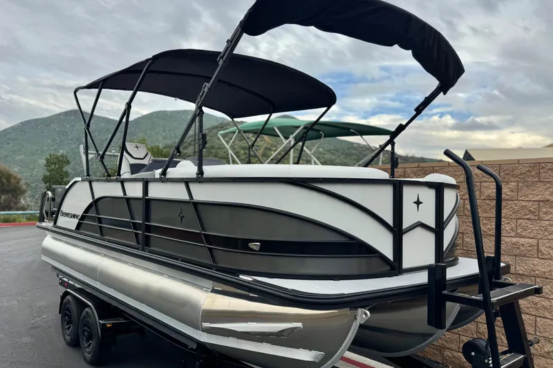 Slide: The Image of 2026 Berkshire 21CL STS pontoon boat with canopy, parked on trailer, scenic mountain backdrop. - 1