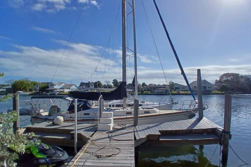 Slide: The Image of 1977 Tartan 37 sailboat docked on a sunny day, surrounded by calm water and houses. - 2