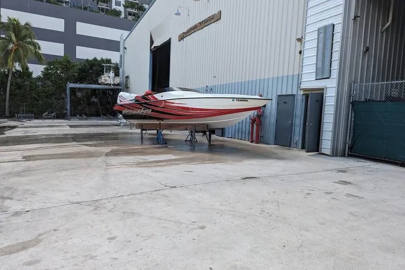 Slide: The Image of 2022 Velocity 290sc speedboat with red and black stripes, displayed on stands outside a marina. - 3