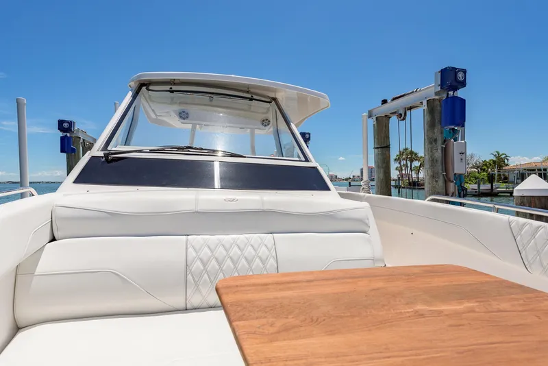 Slide: The Image of 2024 Regal 33 SAV boat interior with white seating and wooden table, docked near waterfront homes. - 28