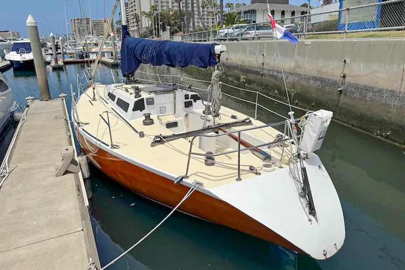 Slide: The Image of 1983 Nelson Marek 36 sailboat docked in a marina, featuring a sleek design and blue sail cover. - 3