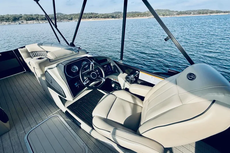 Slide: The Image of 2019 Barletta L23UC boat interior with luxurious seating and steering, on a serene lake. - 21