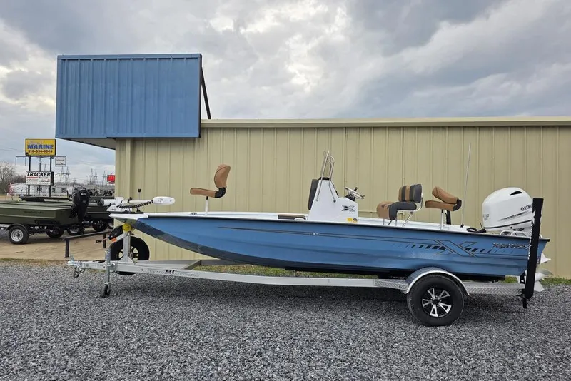 Slide: The Image of 2026 Xpress H20B Bay boat on trailer, parked outside a building under cloudy skies. - 7