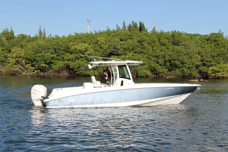 The Image of 2015 Boston Whaler 320 Outrage boat cruising on calm water near lush greenery. - 0