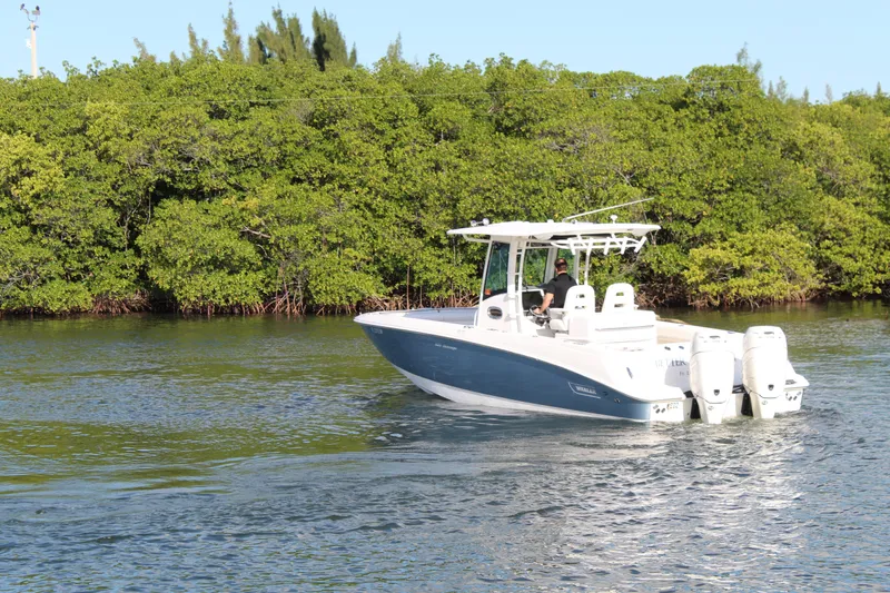 Slide: The Image of 2015 Boston Whaler 320 Outrage boat cruising near lush green shoreline. - 27