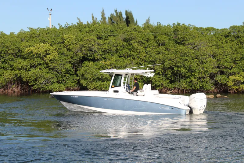 Slide: The Image of 2015 Boston Whaler 320 Outrage boat cruising near lush green shoreline. - 28