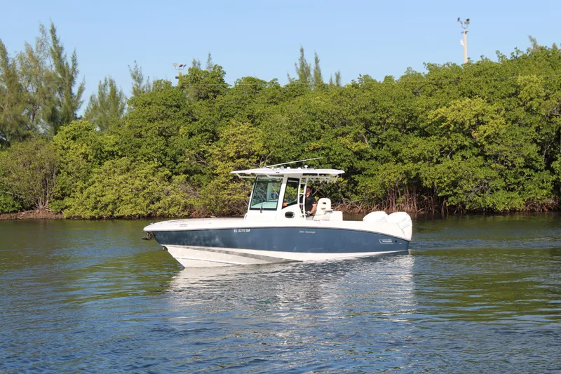 Slide: The Image of 2015 Boston Whaler 320 Outrage boat cruising on calm water near lush greenery. - 29