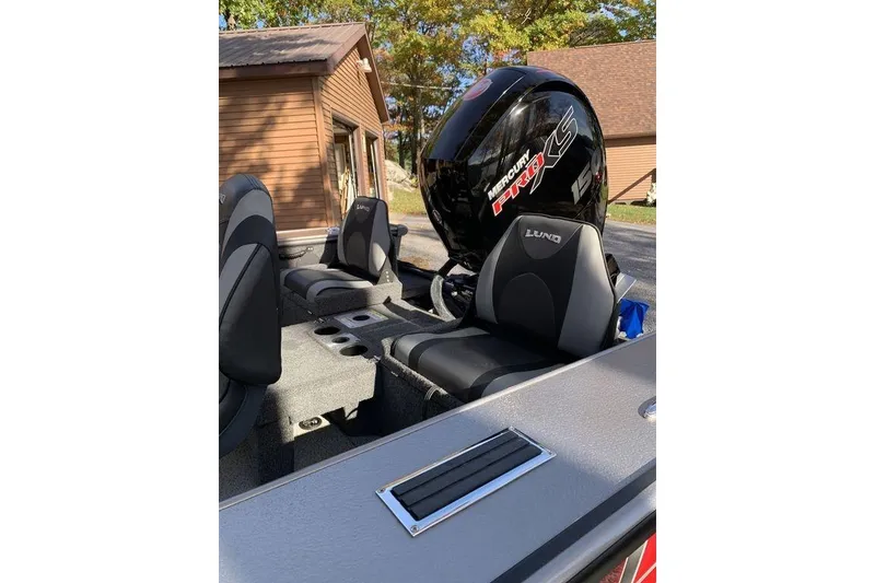 Slide: The Image of 2022 Lund 1875 Pro-V Sport boat interior with Mercury engine, parked near a wooden building. - 4