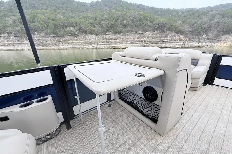 Slide: The Image of 2020 Barletta L23UC pontoon boat interior with table, seating, and scenic lake view. - 23