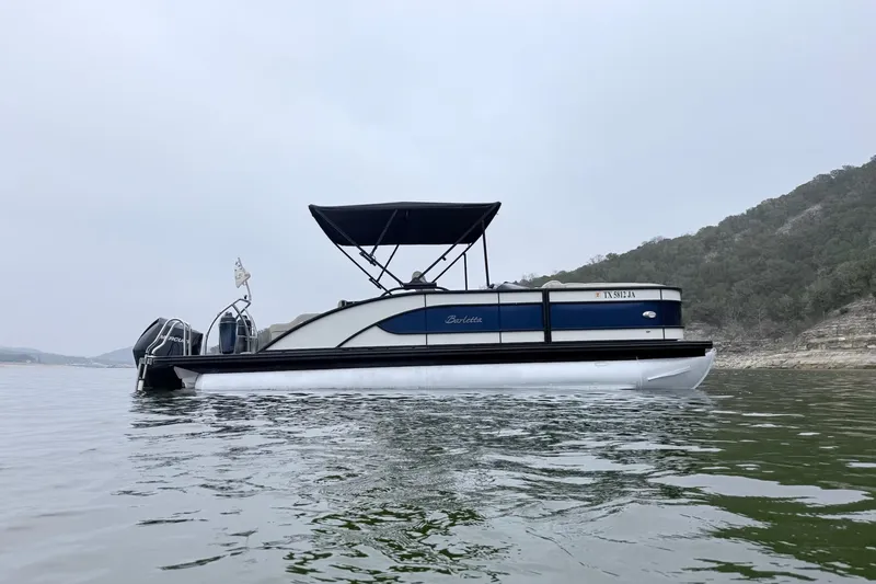Slide: The Image of 2020 Barletta L23UC pontoon boat on calm water with scenic hillside background. - 6