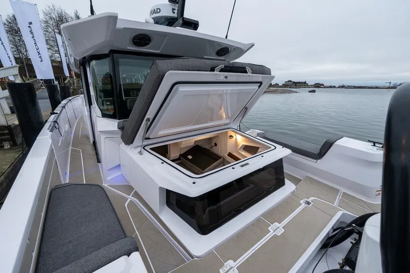 Slide: The Image of 2027 Axopar 38 Cross Cabin boat with open storage compartment, docked by the water. - 12