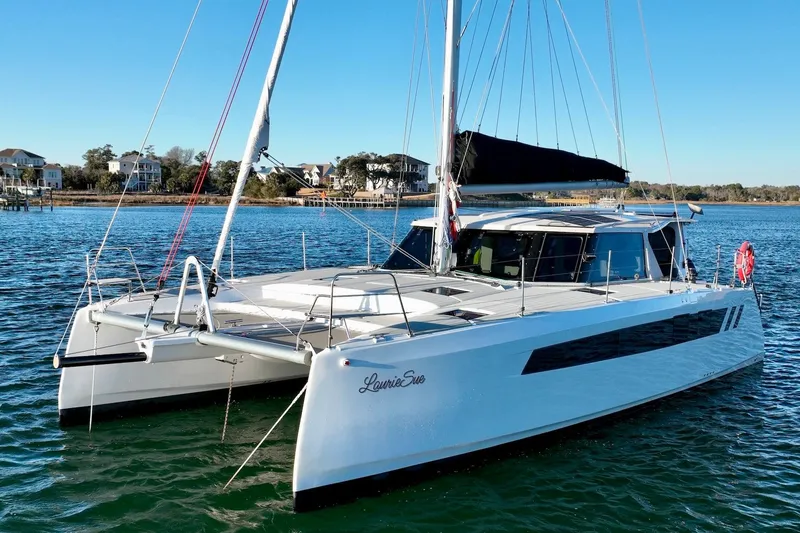 Slide: The Image of 2023 Seawind 1170 catamaran sailing on a sunny day near coastal homes. - 2