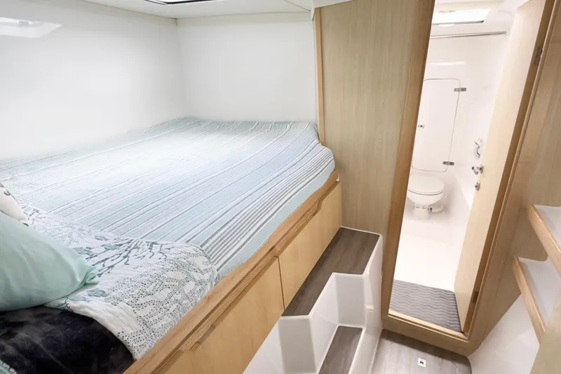 Slide: The Image of 2023 Seawind 1170 cabin interior with bed, wooden accents, and adjacent bathroom. - 33