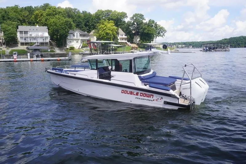 Slide: The Image of 2025 Axopar 29 XC Cross Cabin boat on a scenic lake with houses in the background. - 3