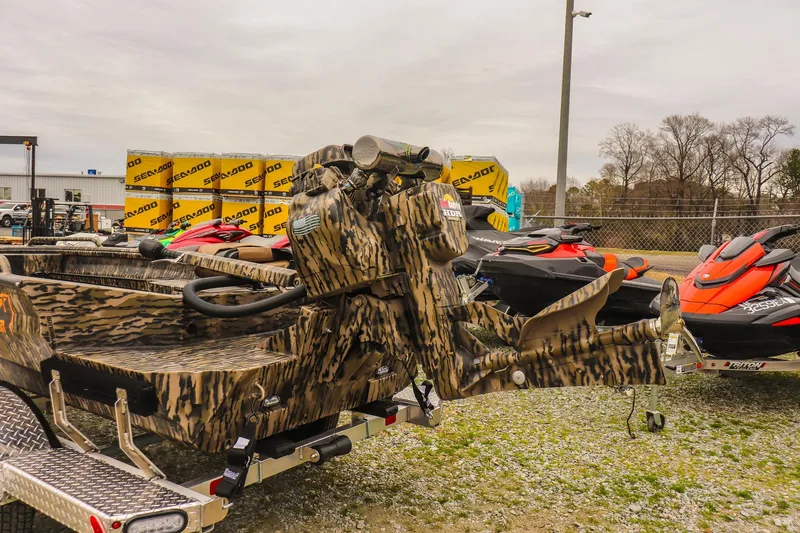 Slide: The Image of 2026 Excel 1751 Shallow Water F4 boat with camouflage design, parked near jet skis. - 11