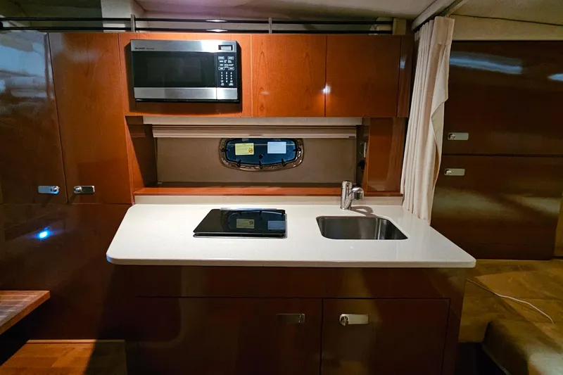 Slide: The Image of 2010 Sea Ray Sundancer 310 galley with microwave, stove, sink, and wooden cabinetry. - 19