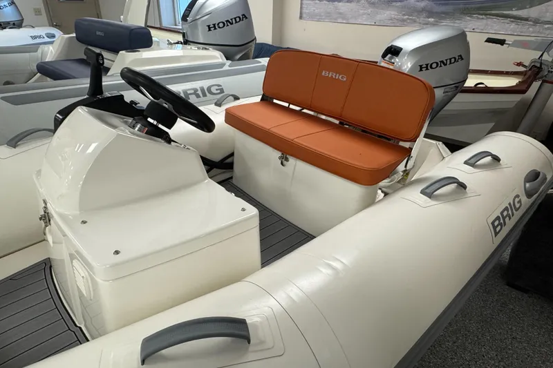 Slide: The Image of 2026 Brig Falcon 330 inflatable boat with Honda engine, featuring orange seating and steering console. - 2