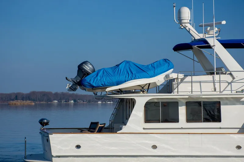 Slide: The Image of Luxury Fleming 55 yacht from 2000 with covered dinghy on deck, serene water backdrop. - 35