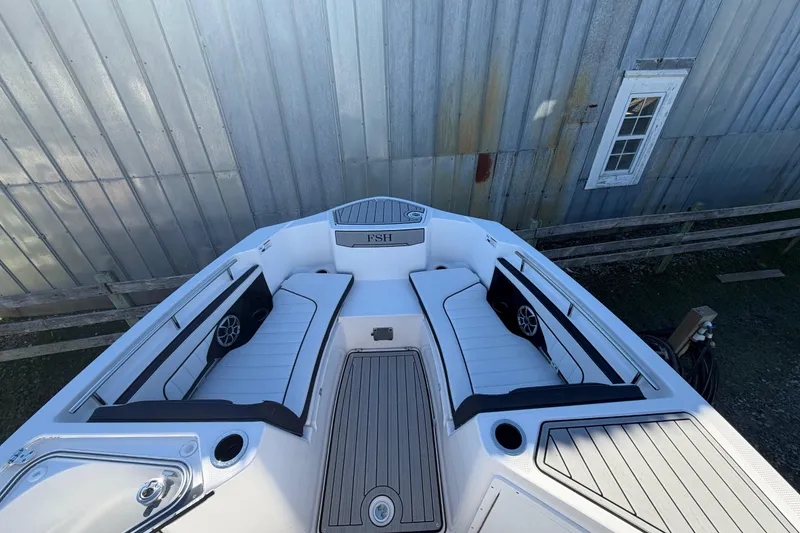 Slide: The Image of 2022 Yamaha Boats 252 FSH Sport interior with seating and speakers, docked near a metal building. - 8